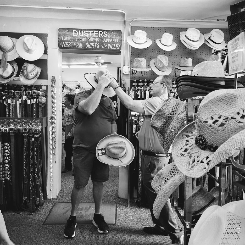 black and white picture of customer trying on western hats