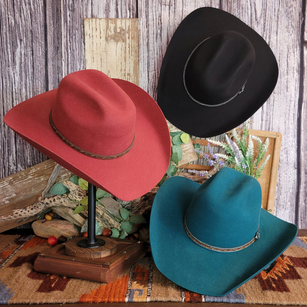 Three cowboy hats in the colors black, turquoise, and carmine featuring decorative leather hat bands.