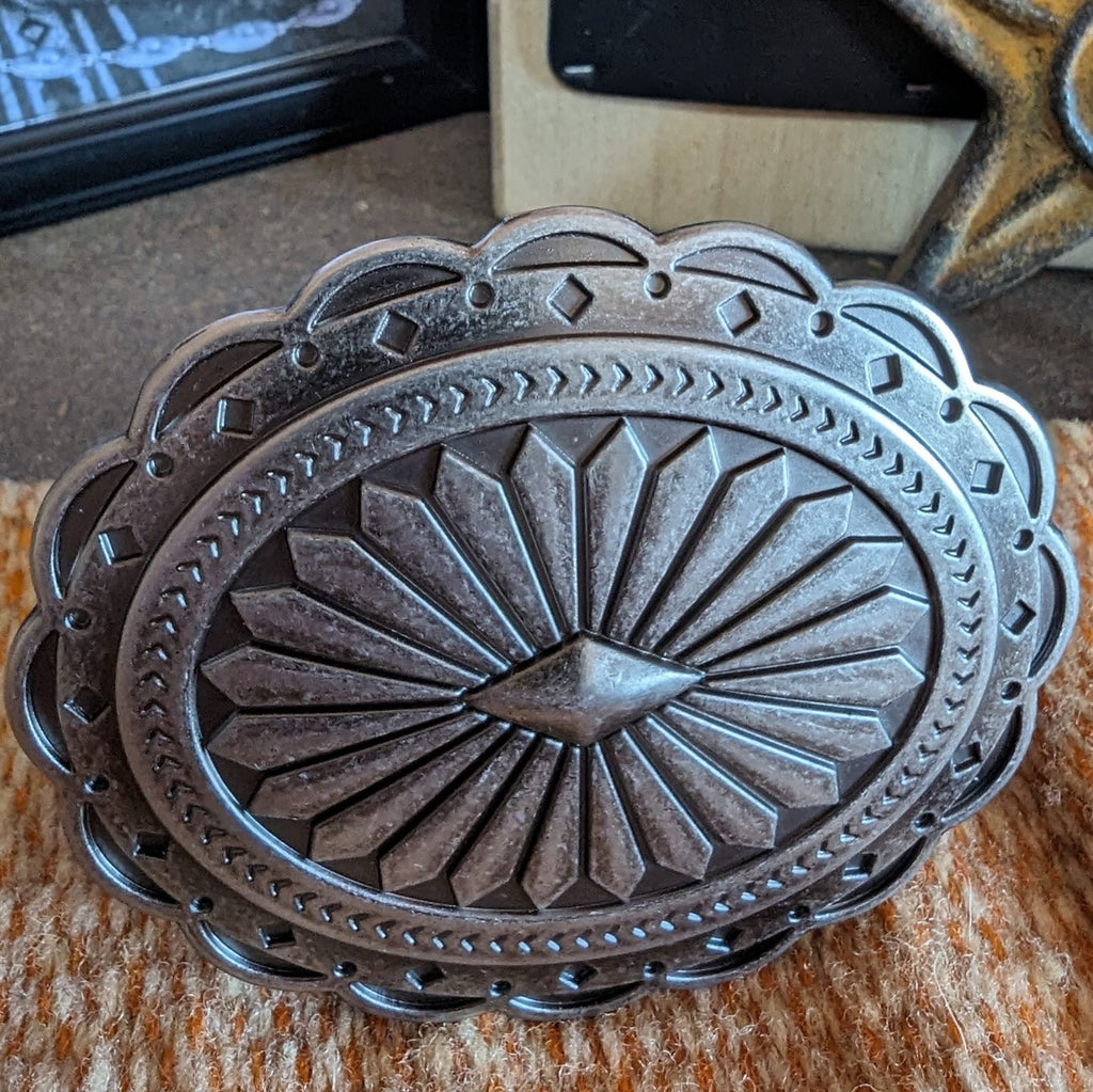 Silver belt buckle with an Aztec oval design, featuring etched patterns and scalloped edges.