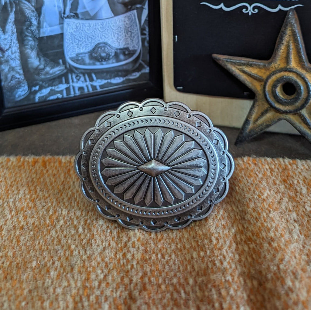 Silver belt buckle with an Aztec oval design, featuring etched patterns and scalloped edges.