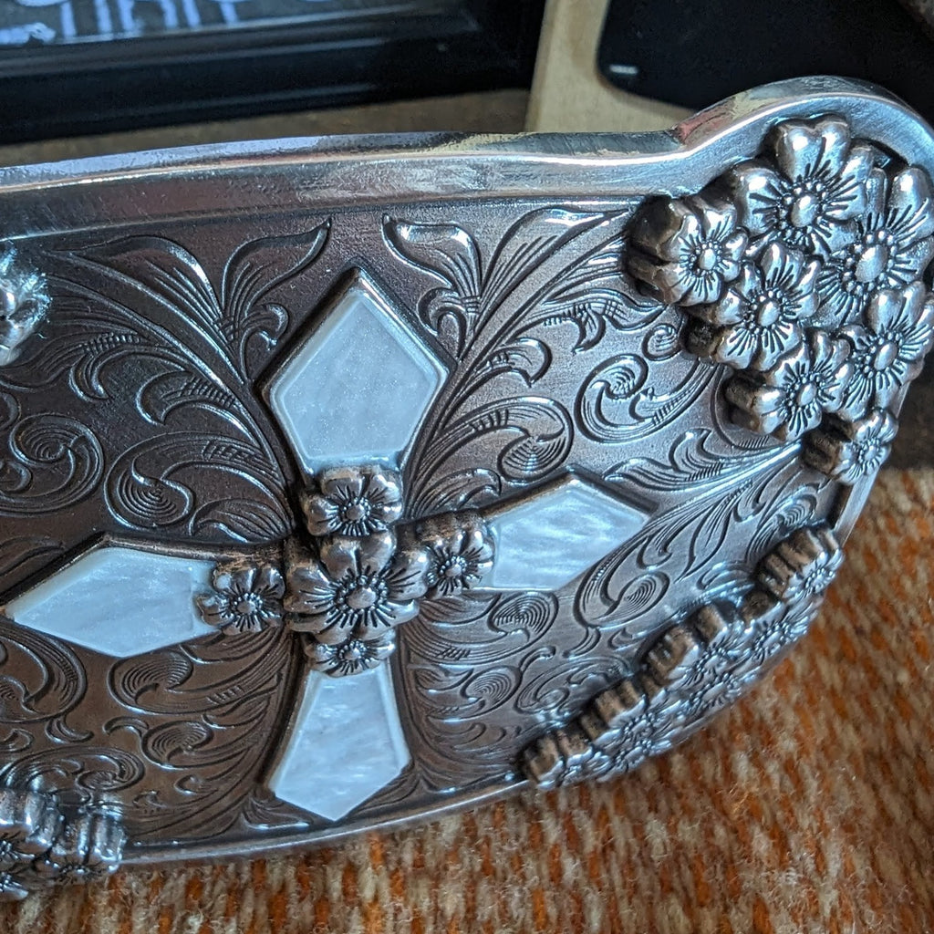 A belt buckle with a cross, framed by tooled floral accents.