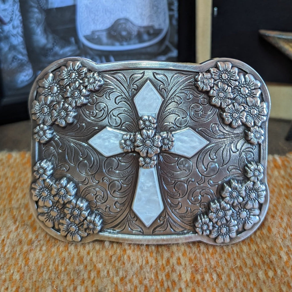 A belt buckle with a cross, framed by tooled floral accents.
