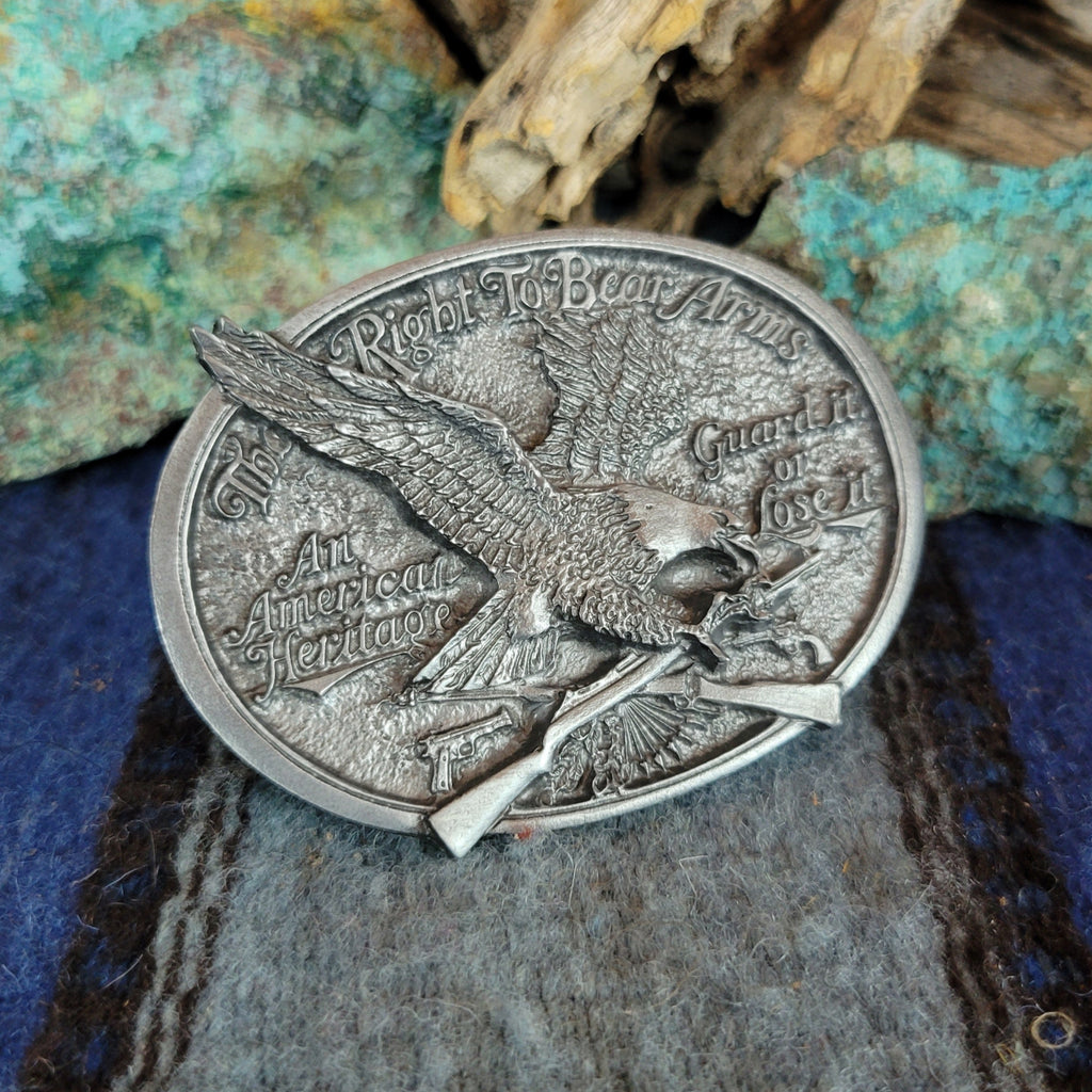 Silver belt buckle with eagle design on a textured surface.