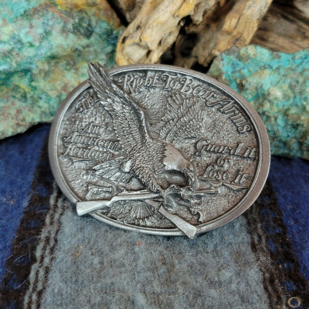 Silver belt buckle with eagle design on a textured surface.