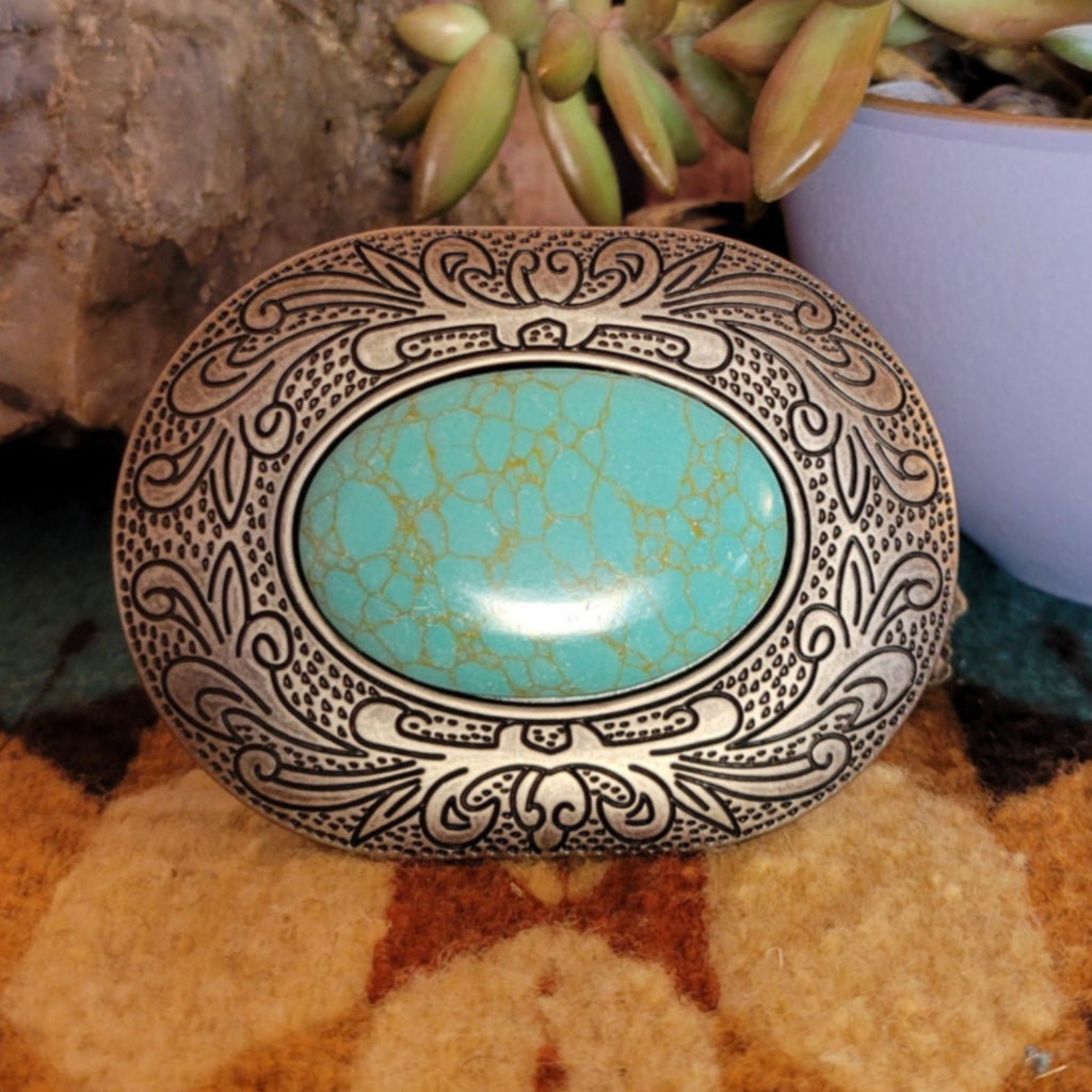 A belt buckle with a large turquoise stone, framed by scrolling silver design.