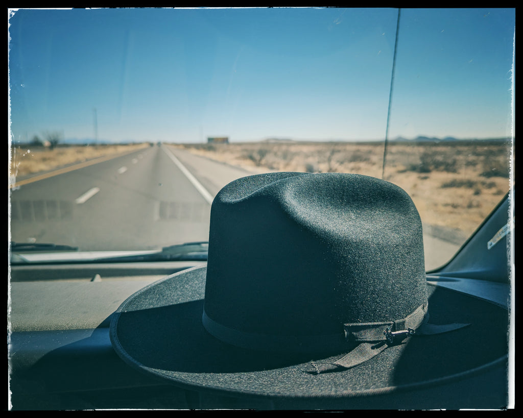 black stetson open road hat on car dashboard with road in the distance