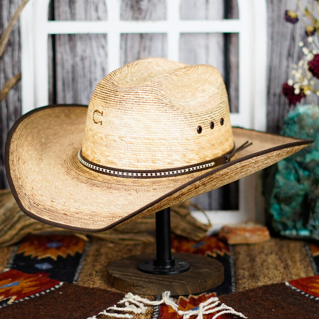 The side profile of the palm hat shows its high crown and wide brim, accented by a dark band with intricate stitching.
