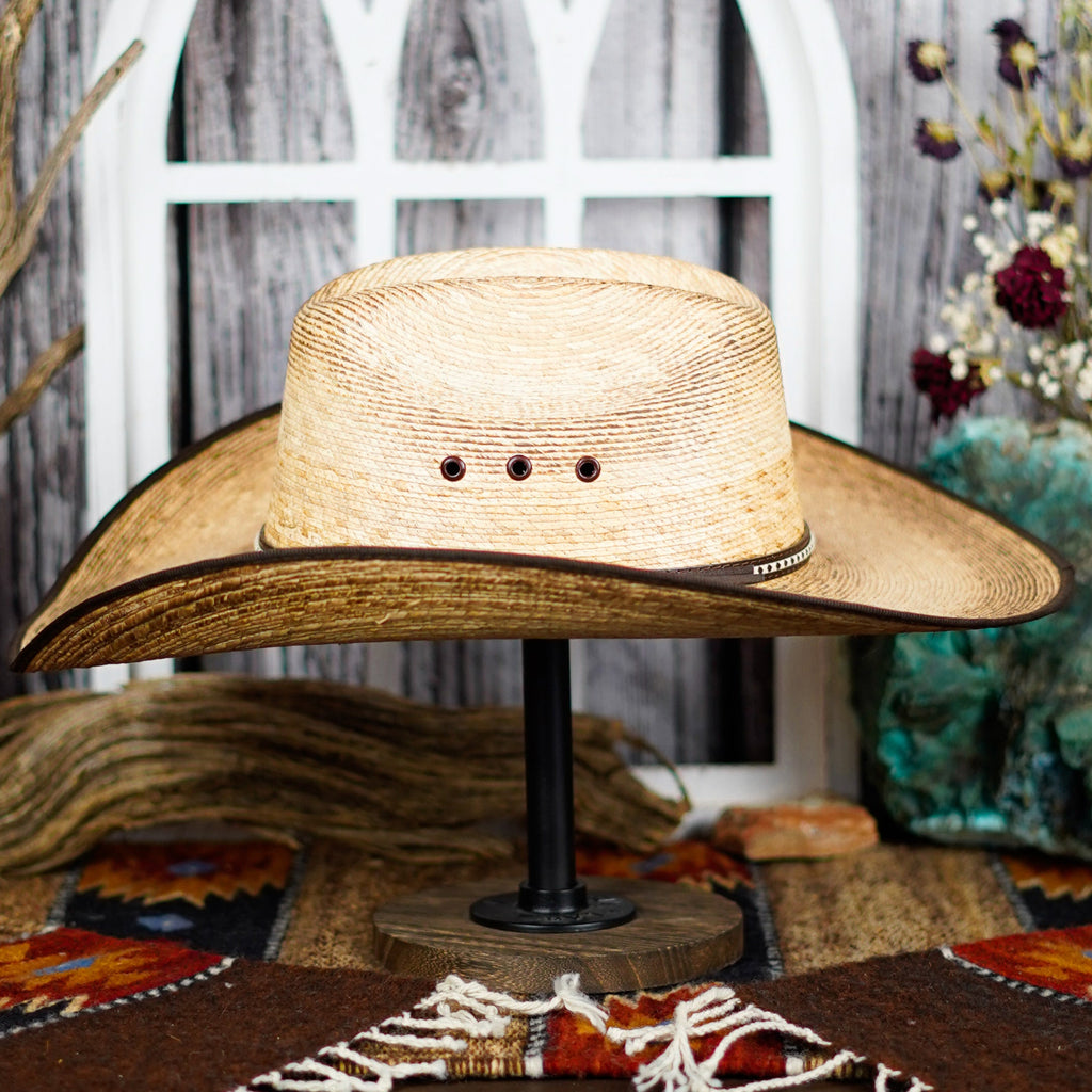 The side profile of the palm hat shows its high crown and wide brim, accented by a dark band with intricate stitching.