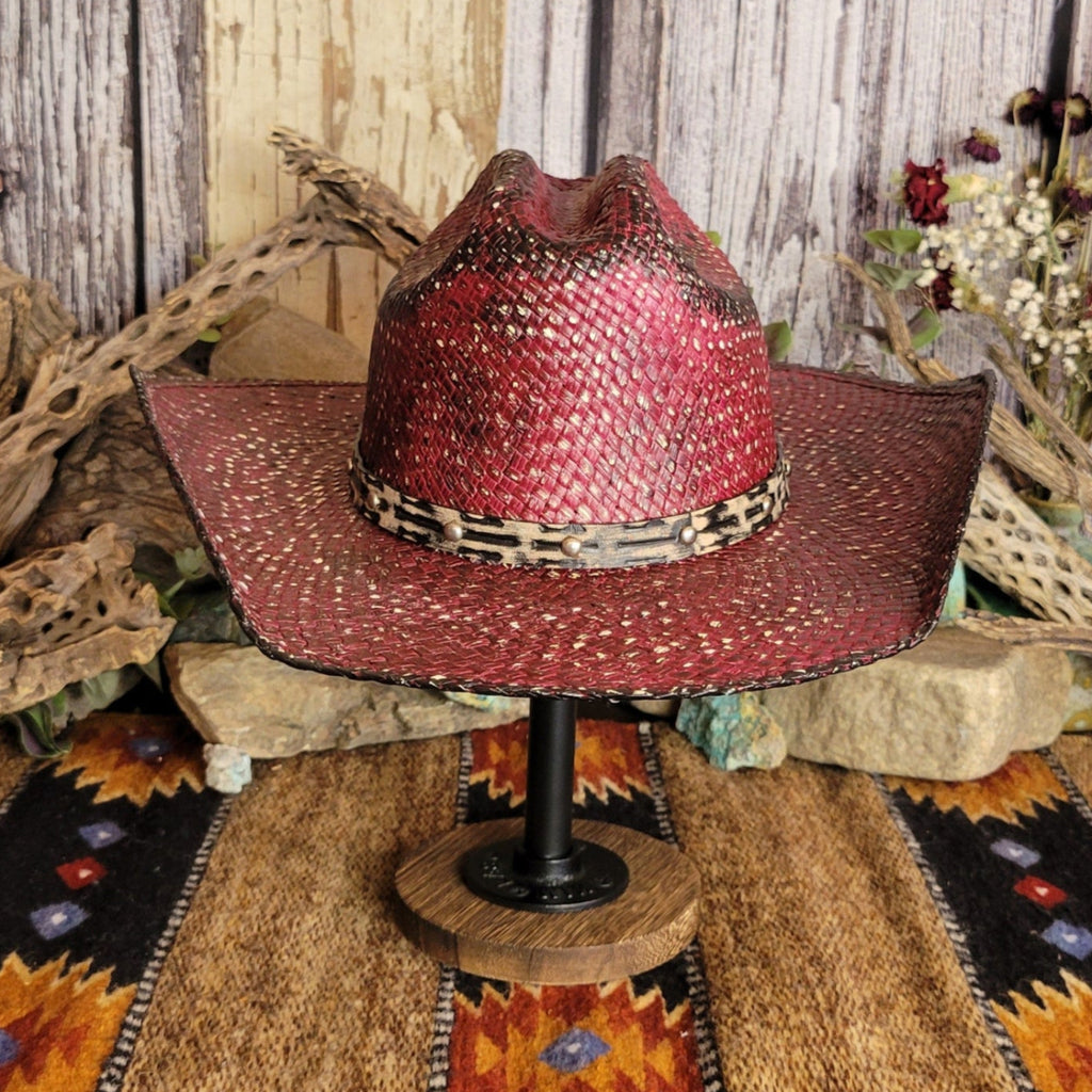A burgundy straw hat with a black-accented weave, featuring a leopard-patterned band with studs.