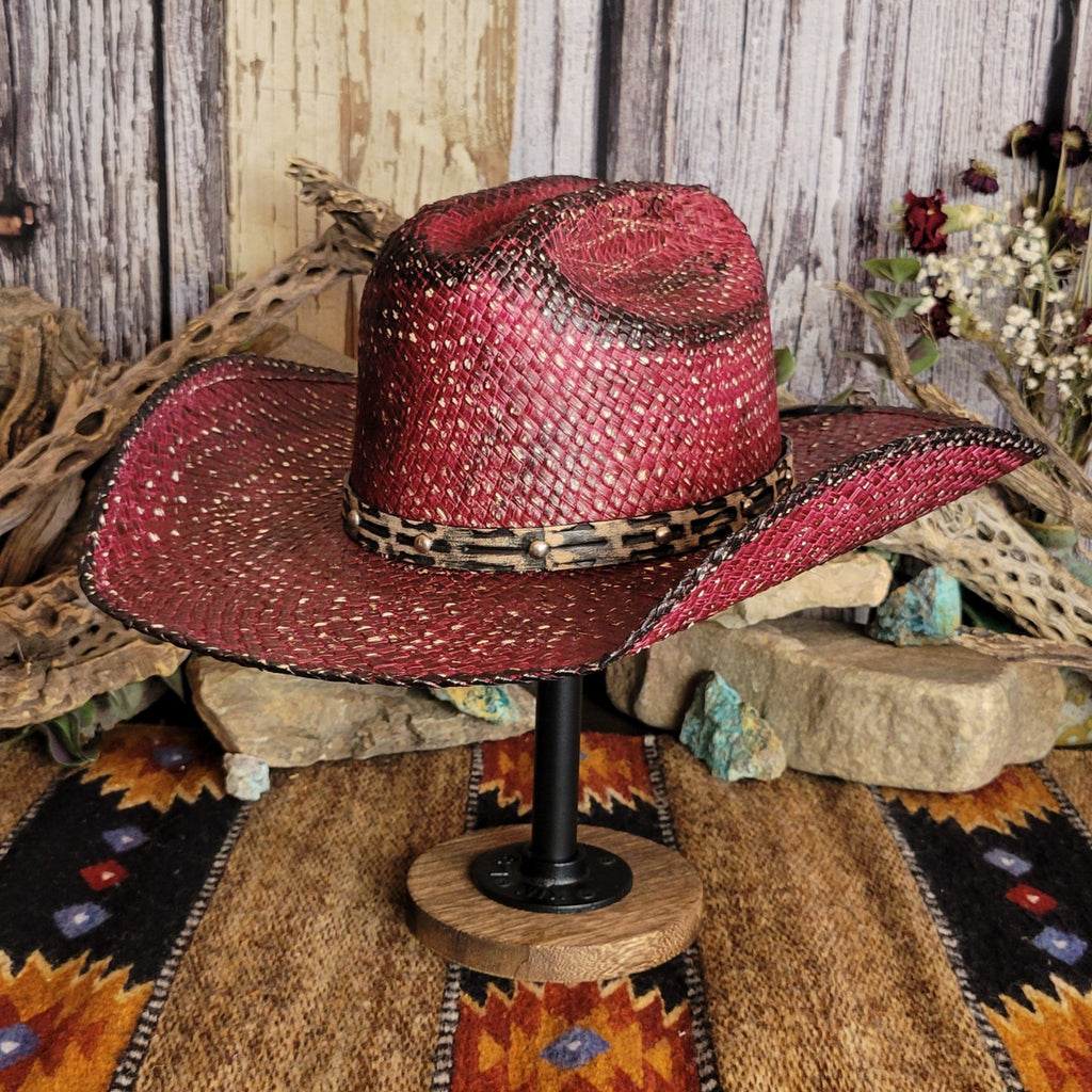 A burgundy straw hat with a black-accented weave, featuring a leopard-patterned band with studs.