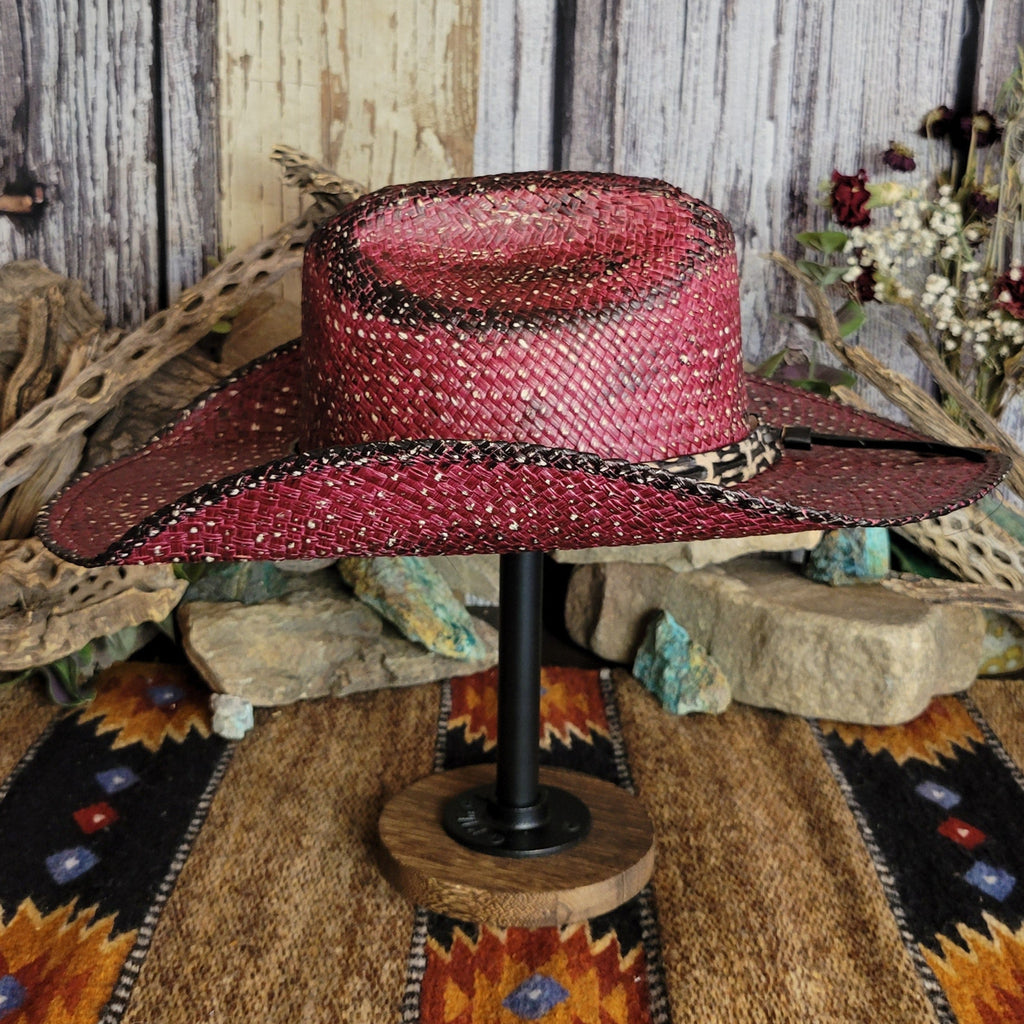 A burgundy straw hat with a black-accented weave, featuring a leopard-patterned band with studs.