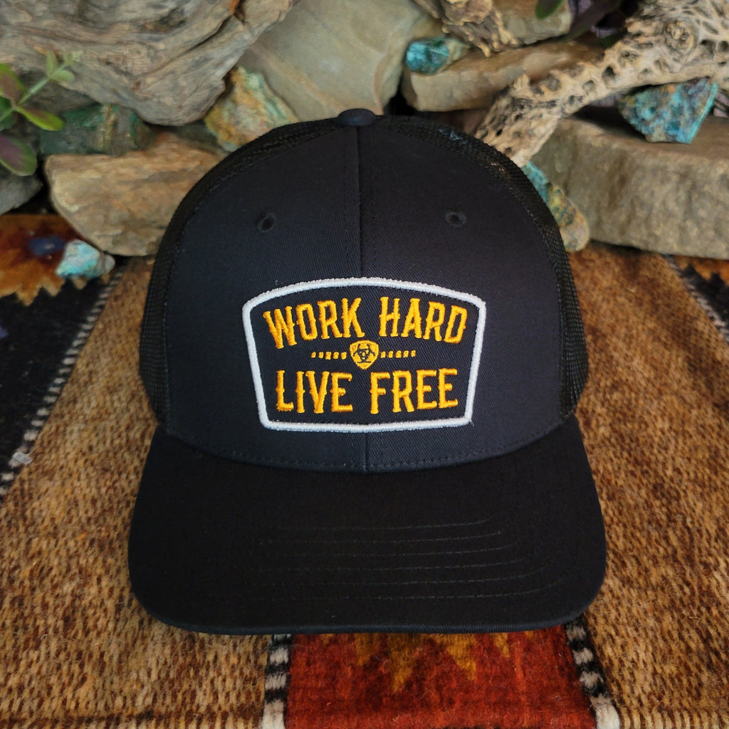 A black trucker cap with a yellow patch and Ariat logo.