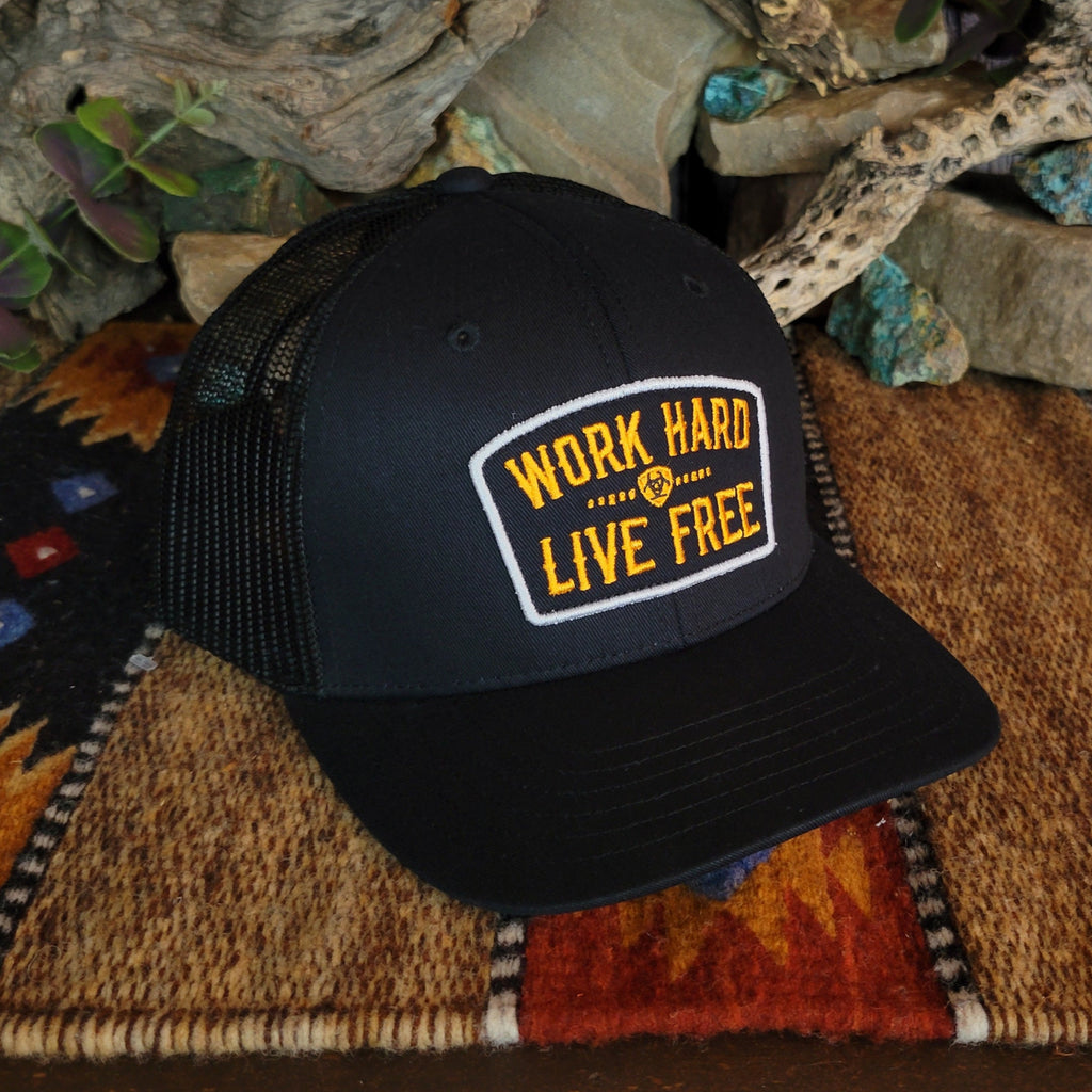 A black trucker cap with a yellow patch and Ariat logo.