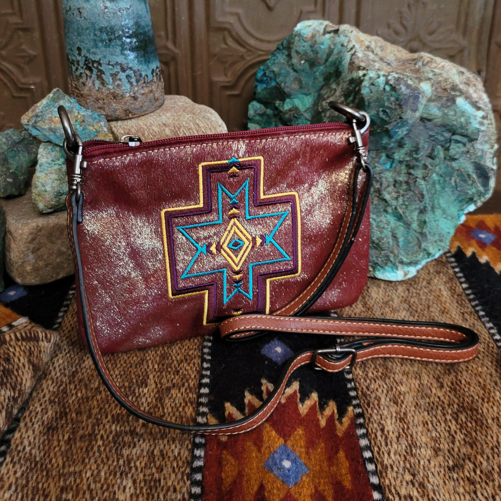 Embroidered clutch with leather accents, vibrant designs and adjustable strap.