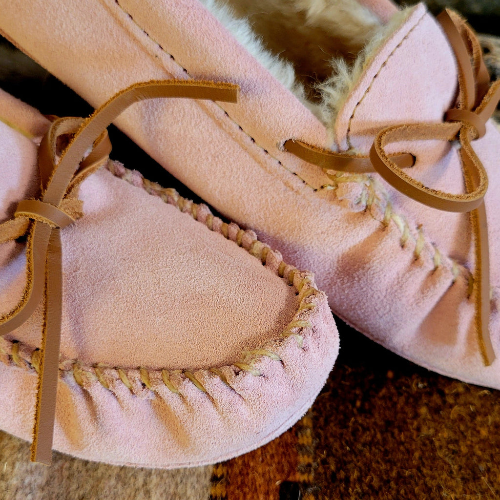 Pair of pink moccasins with pile lined interior, rawhide lace, and soft sole exterior.