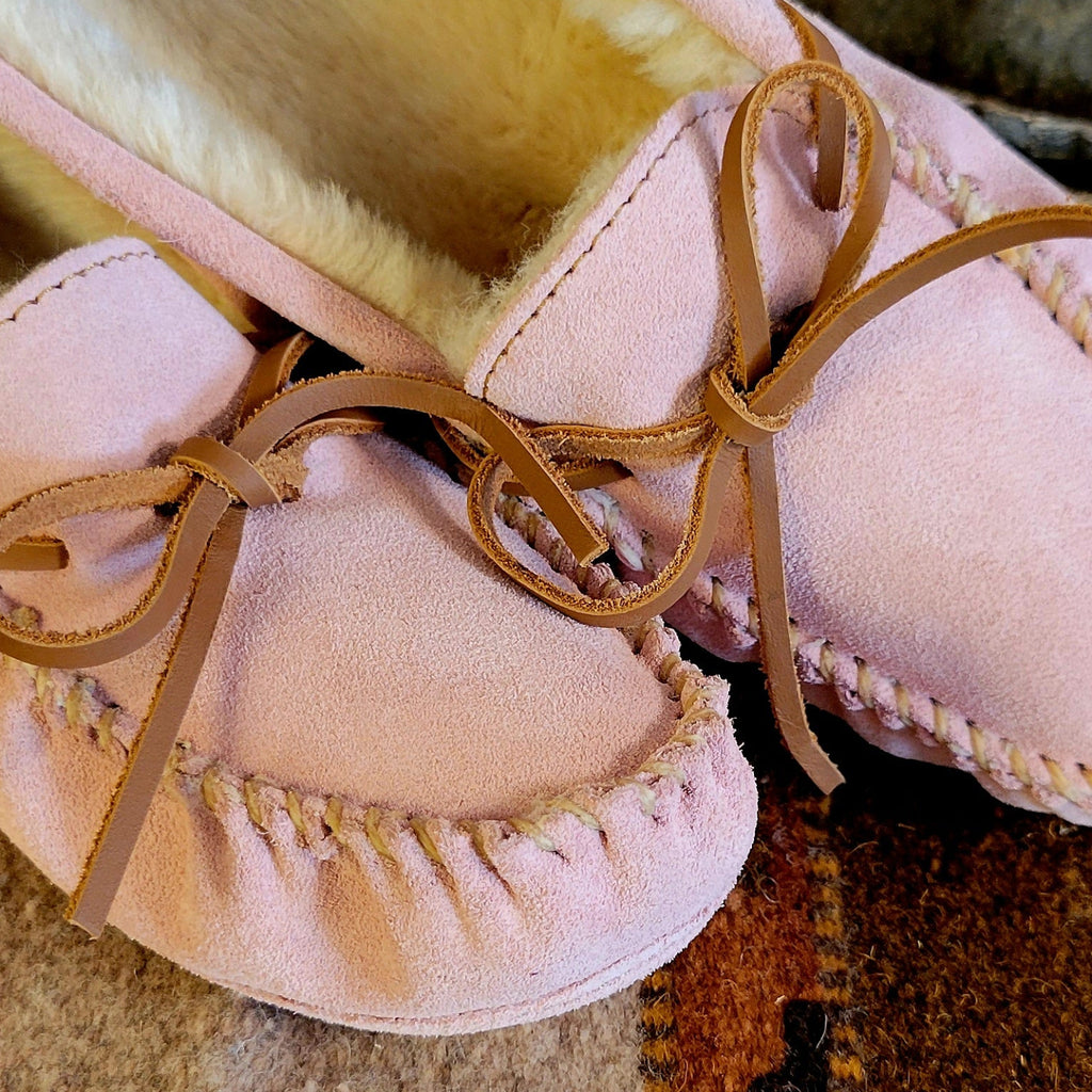 Pair of pink moccasins with pile lined interior, rawhide lace, and soft sole exterior.