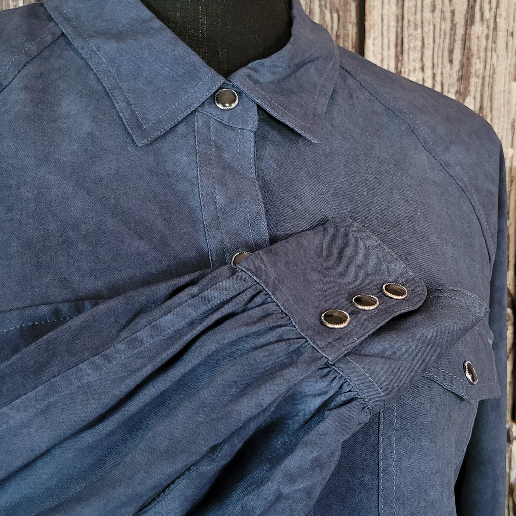 Denim colored long sleeve shirt with snap buttons, dual pockets, and blouse sleeves.