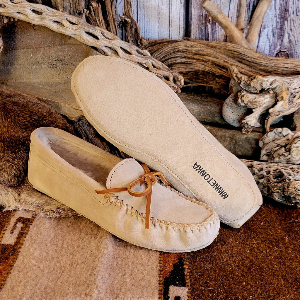 Pair of cream colored moccasins with pile lined interior, rawhide laces, and soft sole exterior.