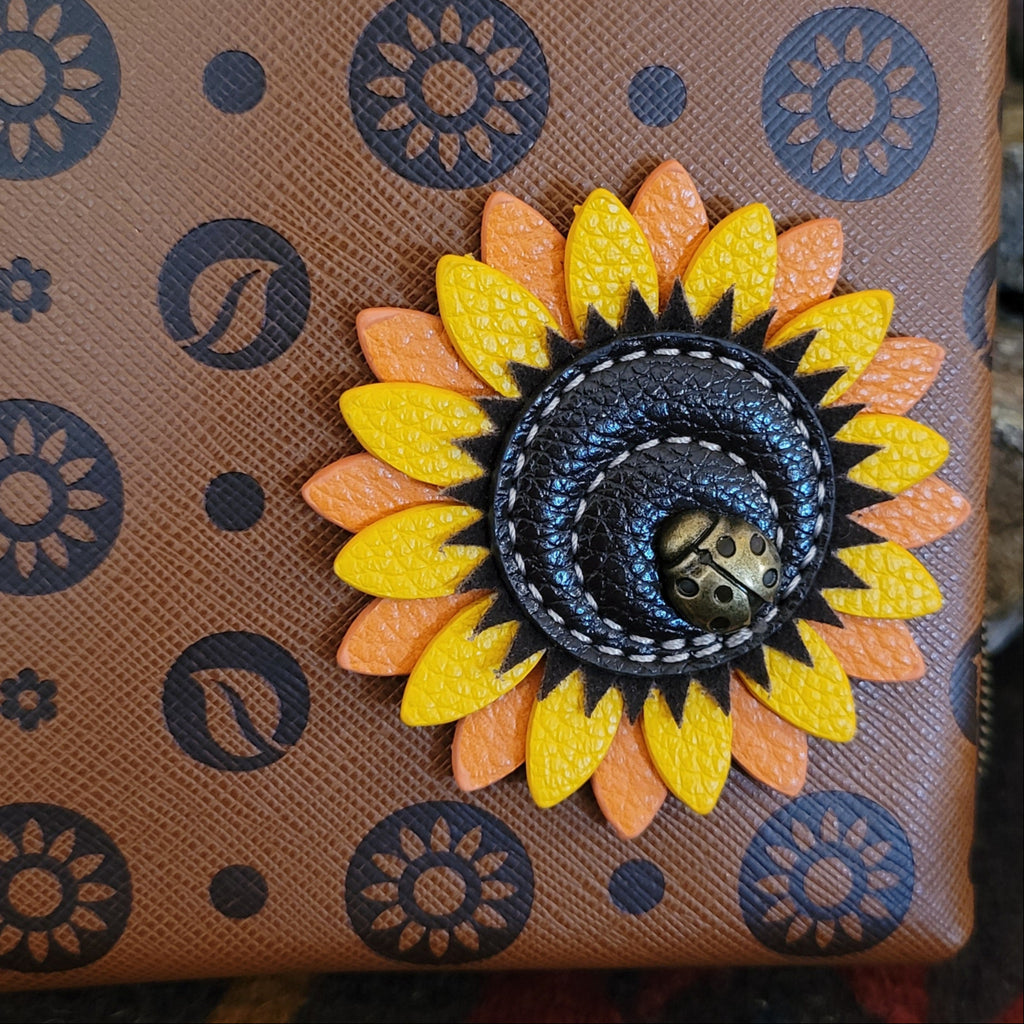 The sunflower’s yellow petals are highlighted with orange stitching, paired with a small ladybug charm at the center.