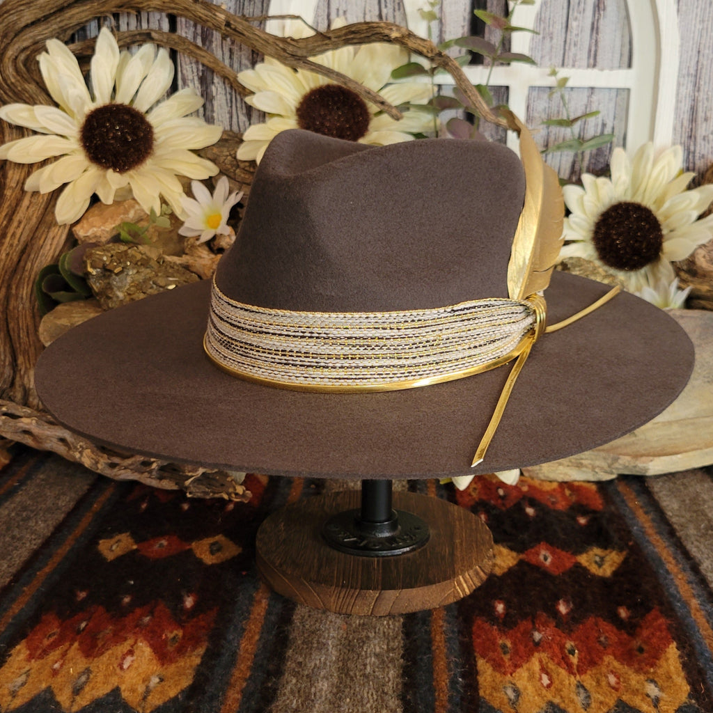 Brown cowgirl hat with decorative tan band and gold feather.