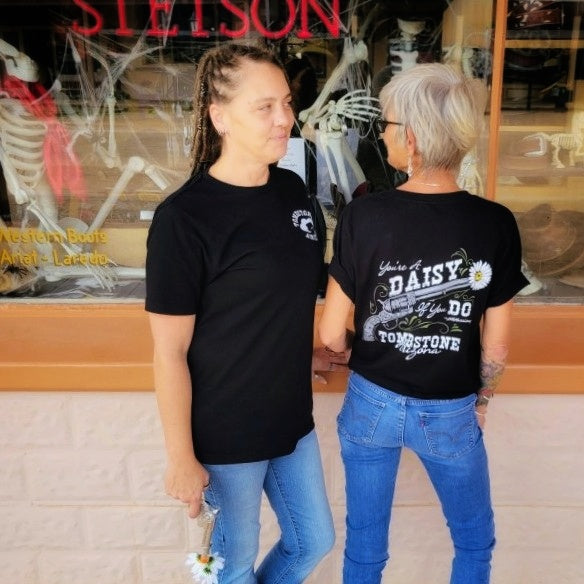 Two women in black 'You're a Daisy If You Do' T-shirts by Black Anchor Supply with daisy revolver graphic on back.
